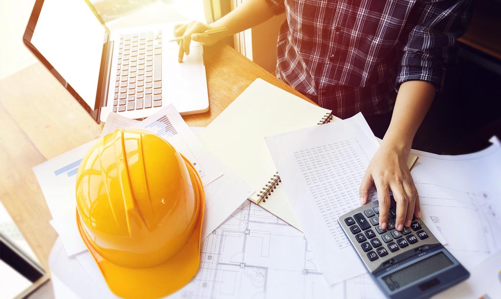 Desk with laptop, calculator and a hard hat