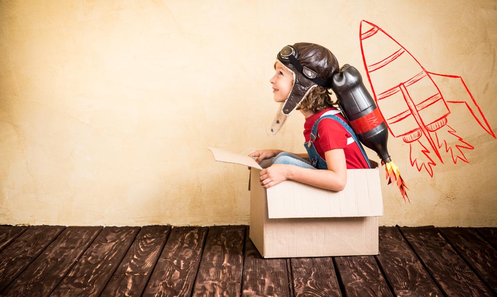 A child sitting in a cardboard box pretending to fly into space